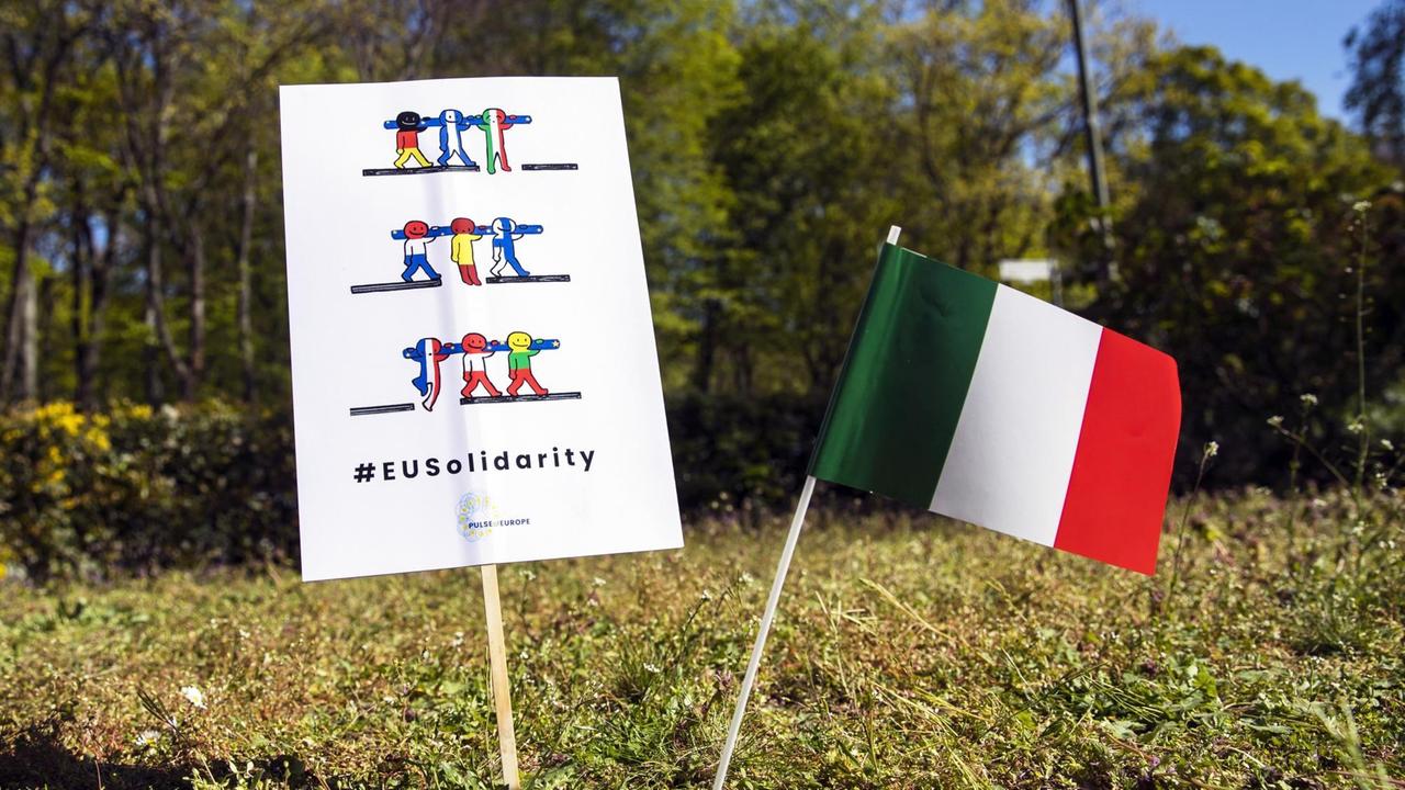 Ein Transparent mit der Aufschrift "Eurosolidarity" und eine italienische Flagge sind während einer Solidaritätsaktion mit Italien vor der italienischen Botschaft in Berlin am 22. April 2020 zu sehen. Auf Initiative von Pulse of Europe, der Europa-Union Berlin, der Jungen Europäischen Bewegung, der Deutsch-Italienischen Parlamentariergruppe im Bundestag und der Vereinigung Deutsch-Italienischer Kulturgesellschaften können Besucher ein großes Transparent mit der Aufschrift "#WeAreInThisTogether, We can only make it together! Ce la faremo solo insieme!' mit eigenen Botschaften gestalten. Ein Transparent mit der Aufschrift "Eurosolidarity" und eine italienische Flagge sind während einer Solidaritätsaktion mit Italien vor der italienischen Botschaft in Berlin am 22. April 2020 zu sehen. Auf Initiative von Pulse of Europe, der Europa-Union Berlin, der Jungen Europäischen Bewegung, der Deutsch-Italienischen Parlamentariergruppe im Bundestag und der Vereinigung Deutsch-Italienischer Kulturgesellschaften können Besucher ein großes Transparent mit der Aufschrift "#WeAreInThisTogether, We can only make it together! Ce la faremo solo insieme!' mit eigenen Botschaften gestalten.