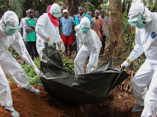 Ebola-Toter wird von Menschen in Schutzanzügen beerdigt.