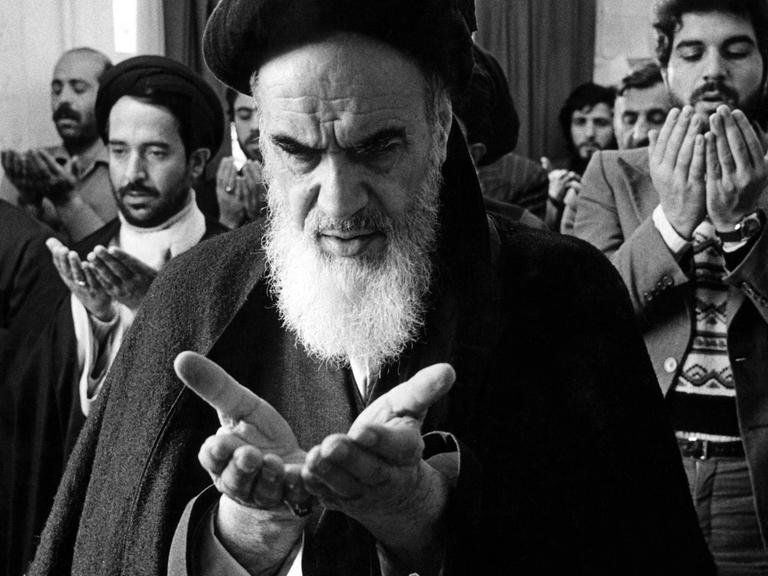 Eine historische sw-Aufnahme zeigt Ayatollah Khomeini inmitten seiner Anhänger beim Gebet in Teheran 1975.
