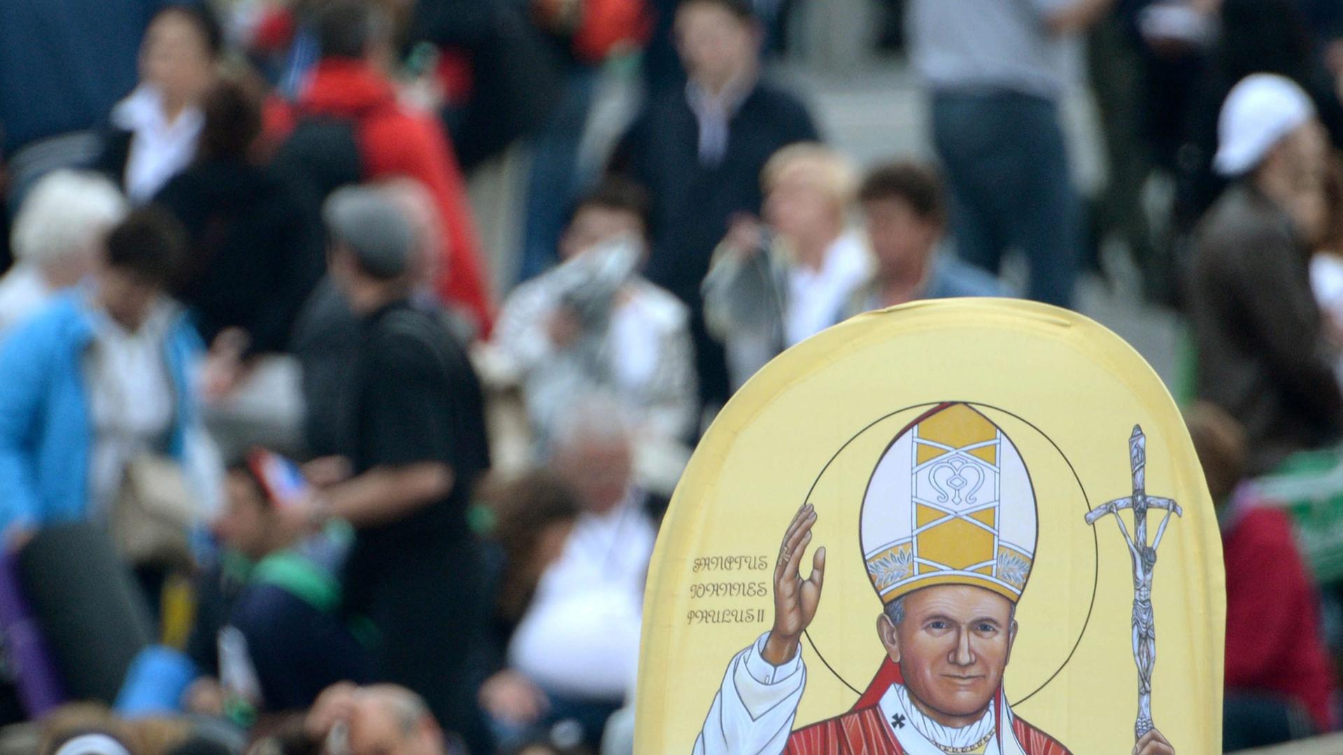 Menschen halten ein Bild von Papst bei dessen Heiligsprechung auf dem Petersplatz in die Höhe. Menschen halten ein Bild von Papst bei dessen Heiligsprechung auf dem Petersplatz in die Höhe.