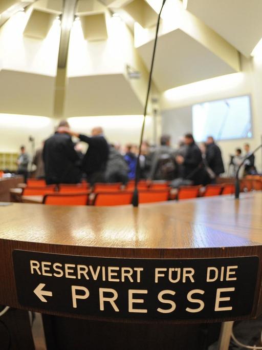Ein Schild markiert die Sitzplätze im Gerichtssaal für Journalisten. Im Hintergrund ist verschwommen der Raum zu sehen.