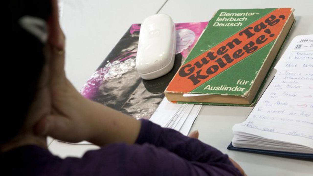 Ein Mädchen sitzt vor einem Schreibtisch mit einem Deutschbuch für Ausländer.