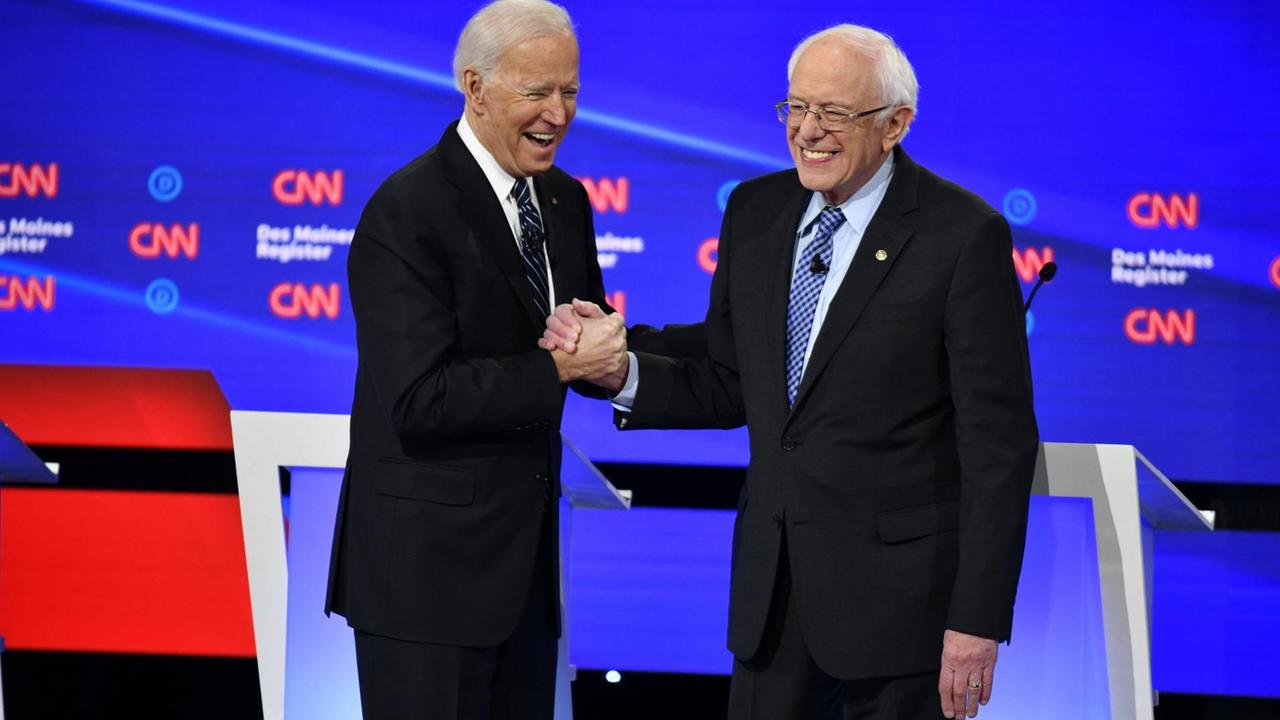 Joe Biden und Bernie Sanders stehen in einer Fernseh-Sendung nebeneinander und reichen sich die Hand. Joe Biden und Bernie Sanders stehen in einer Fernseh-Sendung nebeneinander und reichen sich die Hand.