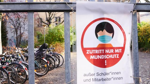 "Zutritt nur mit Mundschutz!" steht auf einem Schild am Eingang zu einer Schule.