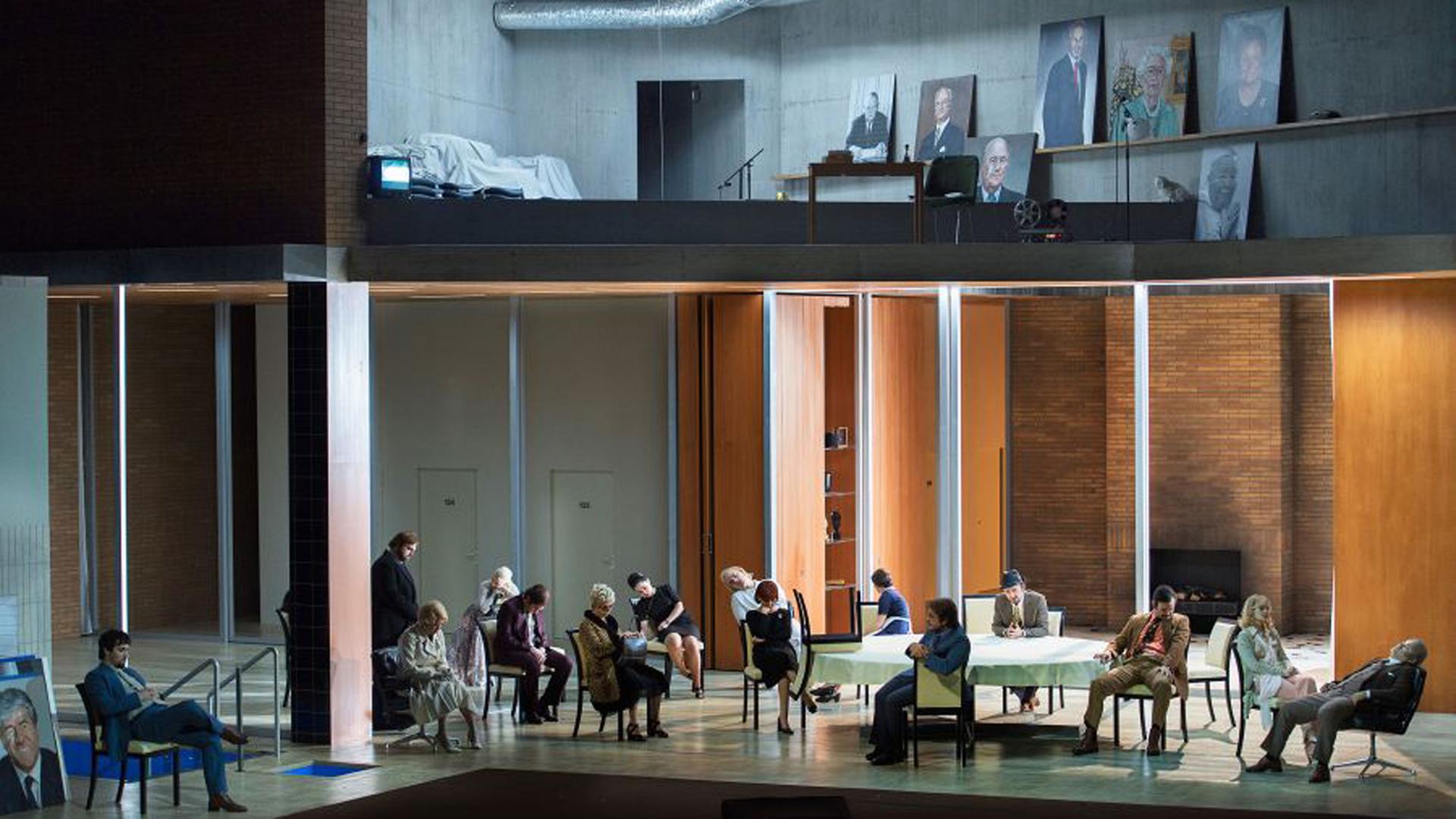 Auf einer zweistöckigen Bühne sitzen im "Erdgeschoss" Schauspieler und Schauspielerinnen wild durcheinander auf Stühlen, teilweise um einen Tisch. An einer Wand lehnt ein Bild des Bankmanagers Josef Ackermann. Im "Obergeschloss" lehnen an kahlen Betonwänden ebenfalls Porträts. Auf einer zweistöckigen Bühne sitzen im "Erdgeschoss" Schauspieler und Schauspielerinnen wild durcheinander auf Stühlen, teilweise um einen Tisch. An einer Wand lehnt ein Bild des Bankmanagers Josef Ackermann. Im "Obergeschloss" lehnen an kahlen Betonwänden ebenfalls Porträts.