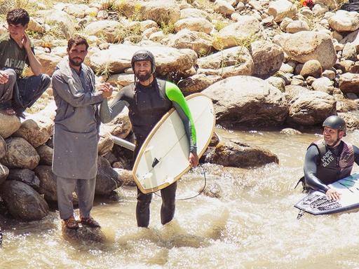 Surfer stehen am Ufer eines Flusses und schütteln einem Afghanen die Hand.