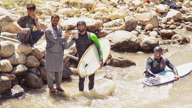 Surfer stehen am Ufer eines Flusses und schütteln einem Afghanen die Hand.