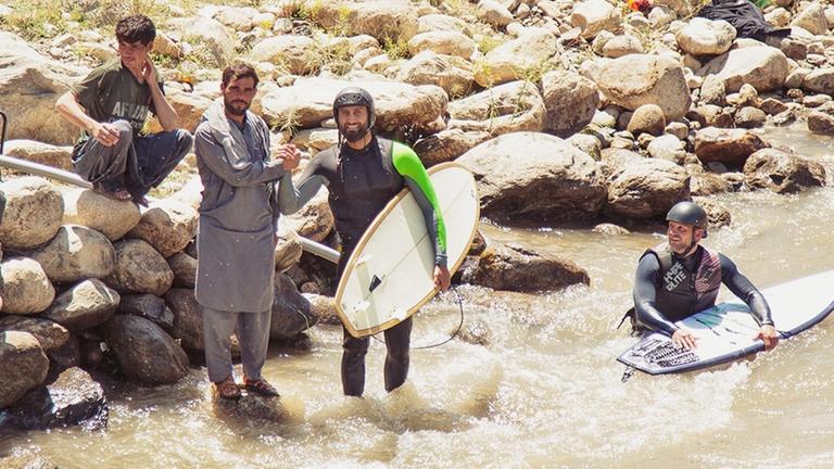 Surfer stehen am Ufer eines Flusses und schütteln einem Afghanen die Hand. Surfer stehen am Ufer eines Flusses und schütteln einem Afghanen die Hand.