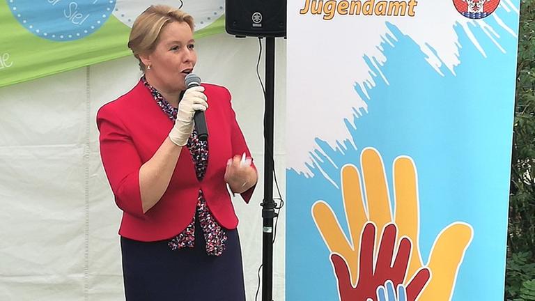 Eine Frau steht vor einer Plakatwand und spricht in ein Mikrofon. Eine Frau steht vor einer Plakatwand und spricht in ein Mikrofon.