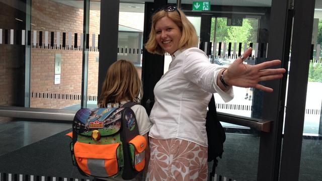 Britta Schwarz geht mit ihrem Sohn durch die tür der Schule und winkt