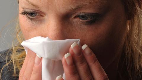 Eine junge Frau putzt sich die Nase.