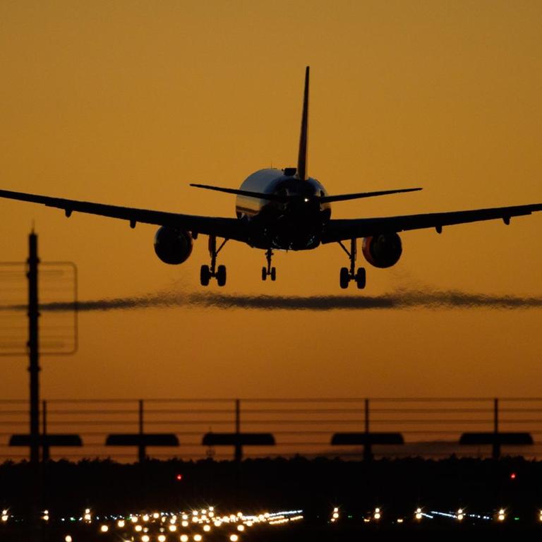 Ein Flugzeug landet auf dem Flughafen Berlin Brandenburg (BER) vor rotem Abendhimmel.