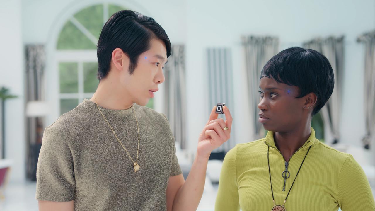 Cee (Lorna Ishema) und Kim (Yung Ngo) stehen sich schräg gegenüber. Kim hält einen kleinen quadratischen Gegenstand vor Cees Gesicht, die ungläubig blickt. An ihren Schläfen leuchten blaue Leuchtdioden. Cee (Lorna Ishema) und Kim (Yung Ngo) stehen sich schräg gegenüber. Kim hält einen kleinen quadratischen Gegenstand vor Cees Gesicht, die ungläubig blickt. An ihren Schläfen leuchten blaue Leuchtdioden.
