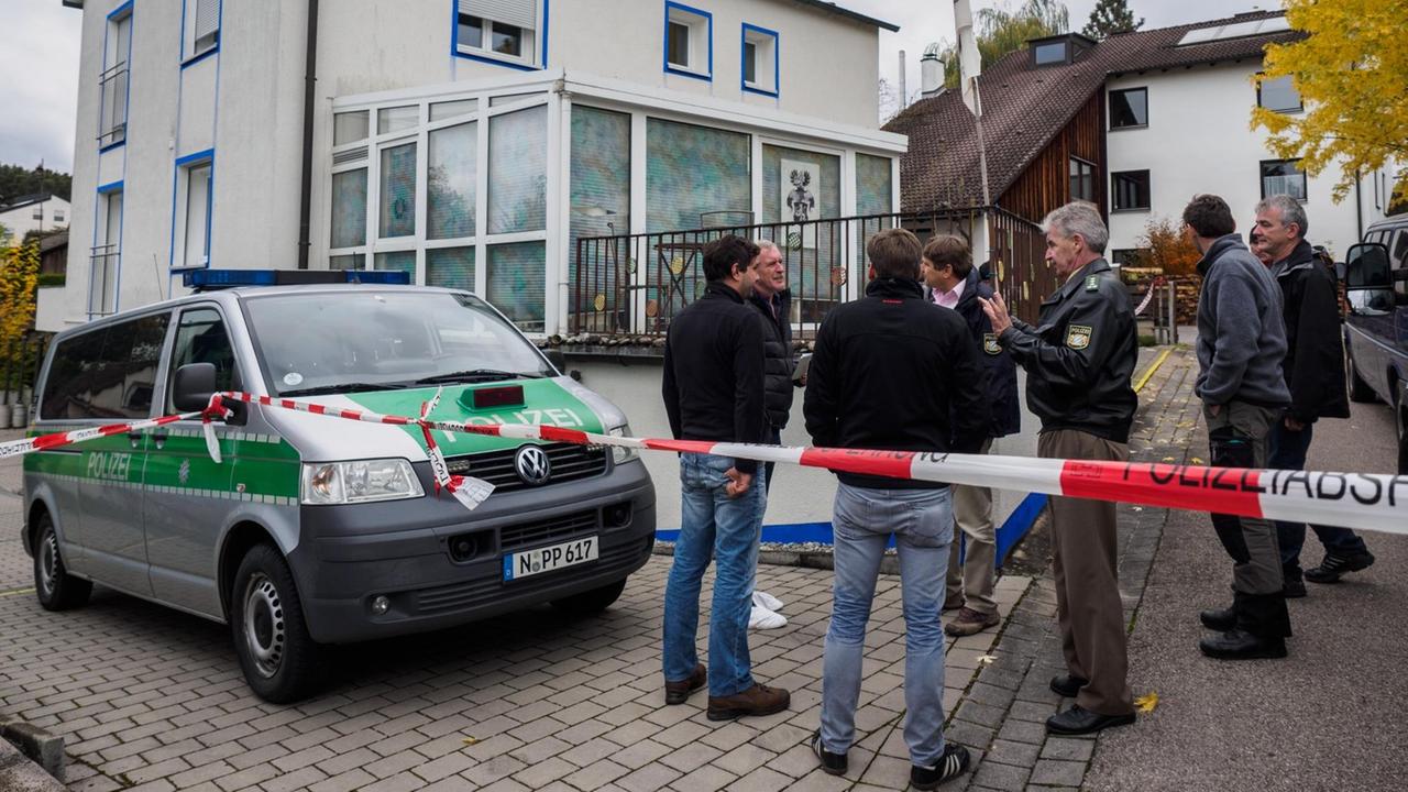 Vor dem abgesperrten weißen Haus steht ein Polizeibus. Daneben unterhalten sich mehrere Polizisten und Ermittler. Vor dem abgesperrten weißen Haus steht ein Polizeibus. Daneben unterhalten sich mehrere Polizisten und Ermittler.