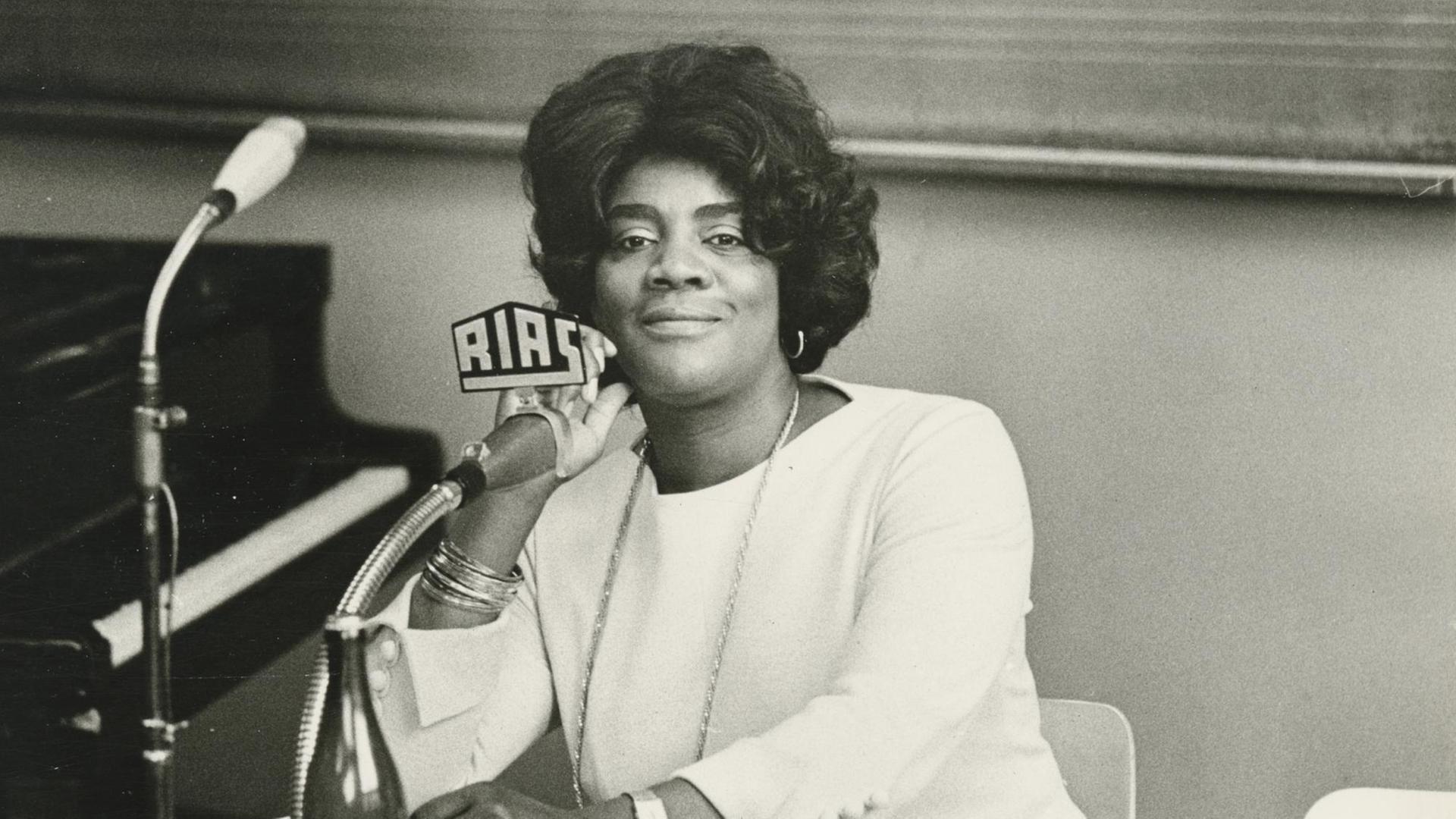 Schwarz-Weiß-Aufnahme der afroamerikanischen Opernsängerin Vera Little in weißer Kleidung vor einem RIAS-Mikrofon.