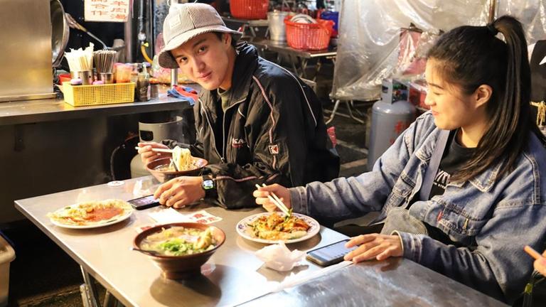 Ein asiatischer Mann und eine asiatische Frau essen auf dem Nachtmarkt in Taipeh mit Stäbchen