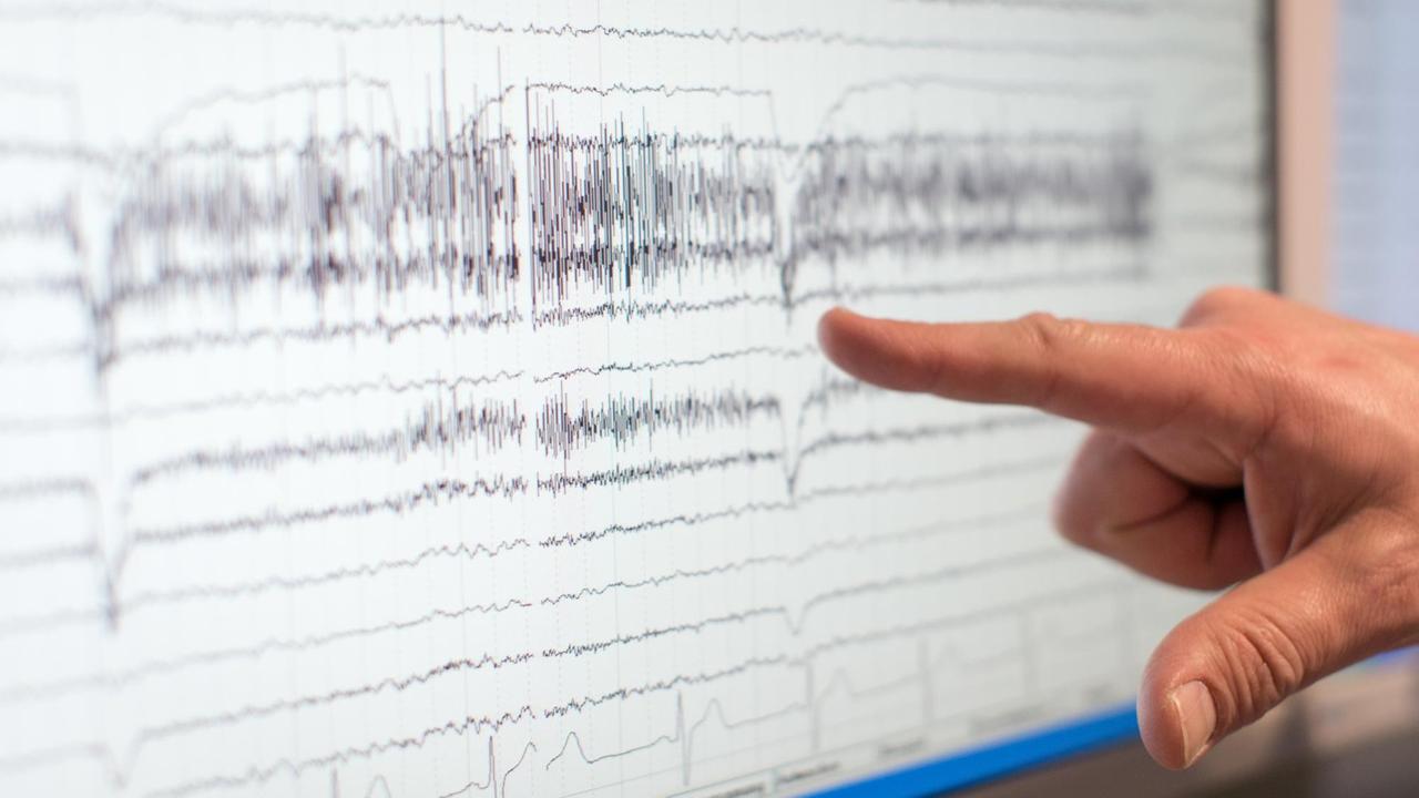 Eine Hand zeigt auf Gehirnströme (EEG), die auf einem Monitor abgebildet werden. Eine Hand zeigt auf Gehirnströme (EEG), die auf einem Monitor abgebildet werden.