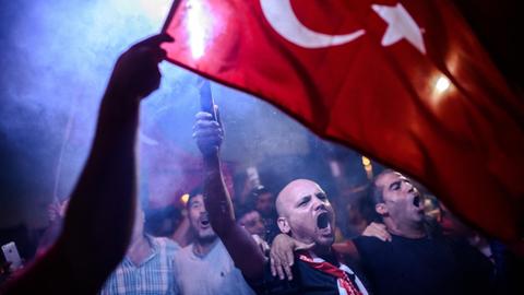 Männer in einer Menschenmenge in der Dunkelheit. Sie rufen und schwenken die türkische Flagge.