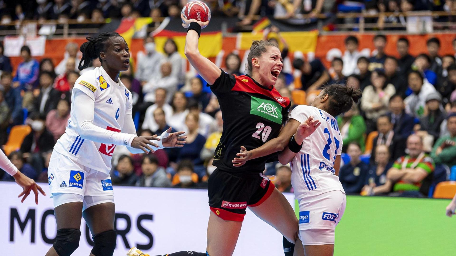 Die deutsche Handball-Nationalspielerin Emily Bölk versucht den ball zu werfen. Die französische Nationalspielerin Estelle Nze Minko versucht sie daran zu hindern.