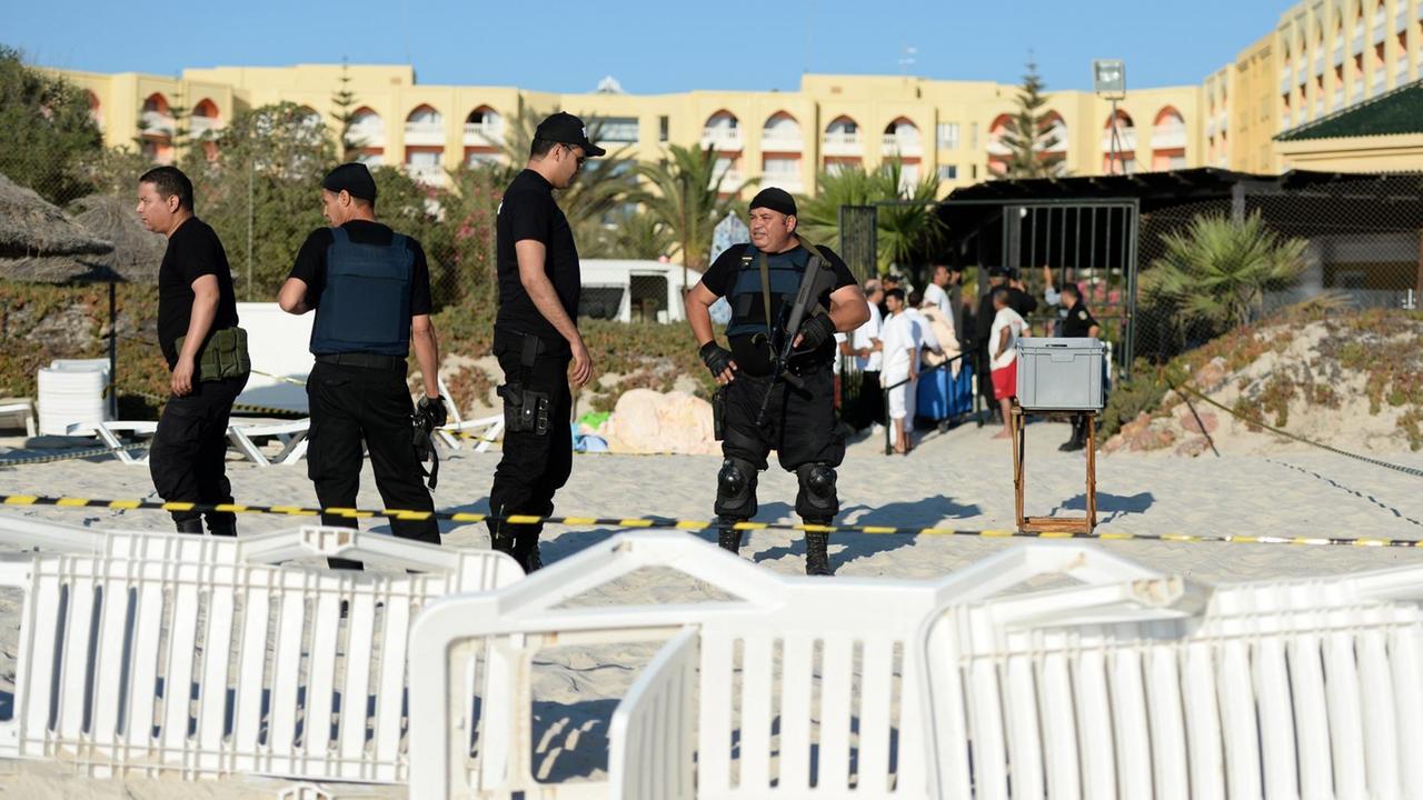 Vier schwarzgekleidete Polizisten stehen einen Tag nach dem Attentat am Strand vor dem Hotel Imperial Marhaba: Die Polizisten tragen Schusswesten. Im Vordergrund sieht man umgestürzte Liegestühle. Vier schwarzgekleidete Polizisten stehen einen Tag nach dem Attentat am Strand vor dem Hotel Imperial Marhaba: Die Polizisten tragen Schusswesten. Im Vordergrund sieht man umgestürzte Liegestühle.