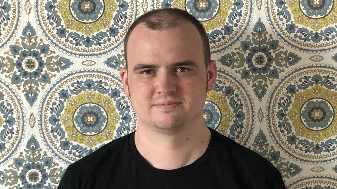 Der Künstler Tobias Vogel steht vor einer stark gemusterten Tapete und schaut skeptisch in die Kamera. Der Künstler Tobias Vogel steht vor einer stark gemusterten Tapete und schaut skeptisch in die Kamera.