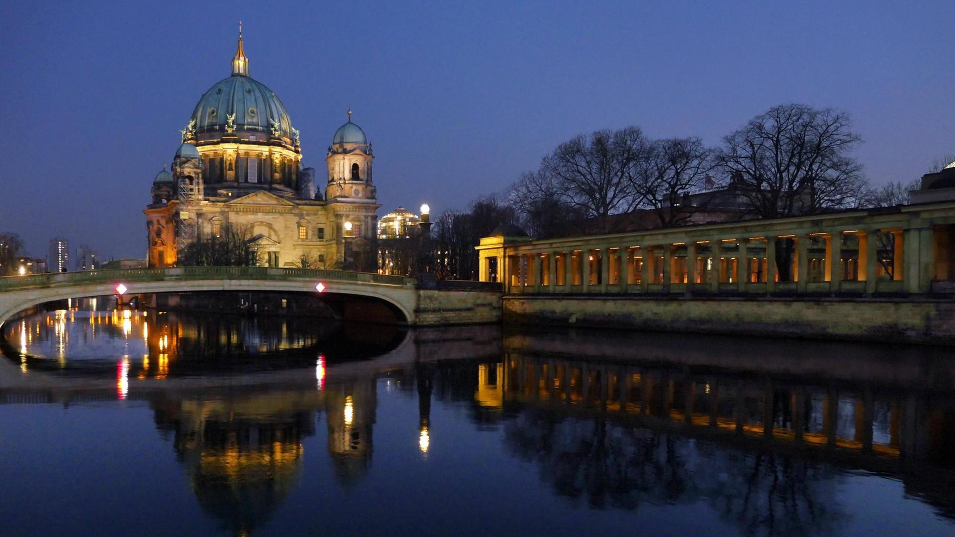 Der Berliner Dom spiegelt sich bei dunklem Himmel im Wasser der Spree. 