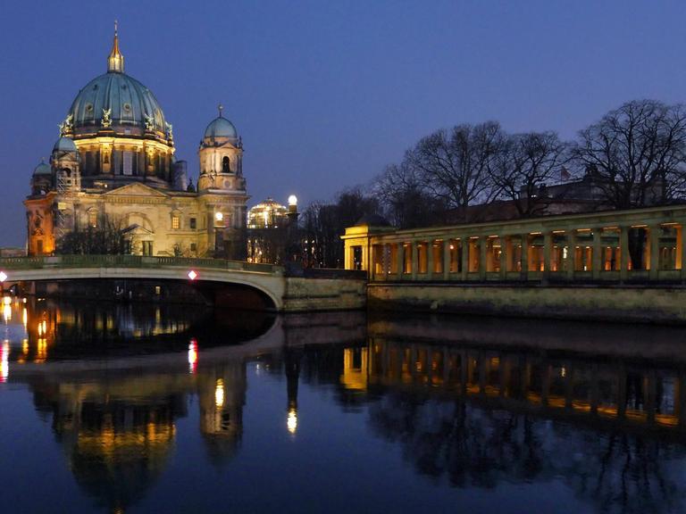 Der Berliner Dom spiegelt sich im Wasser der Spree bei nächtlicher Beleuchtung.