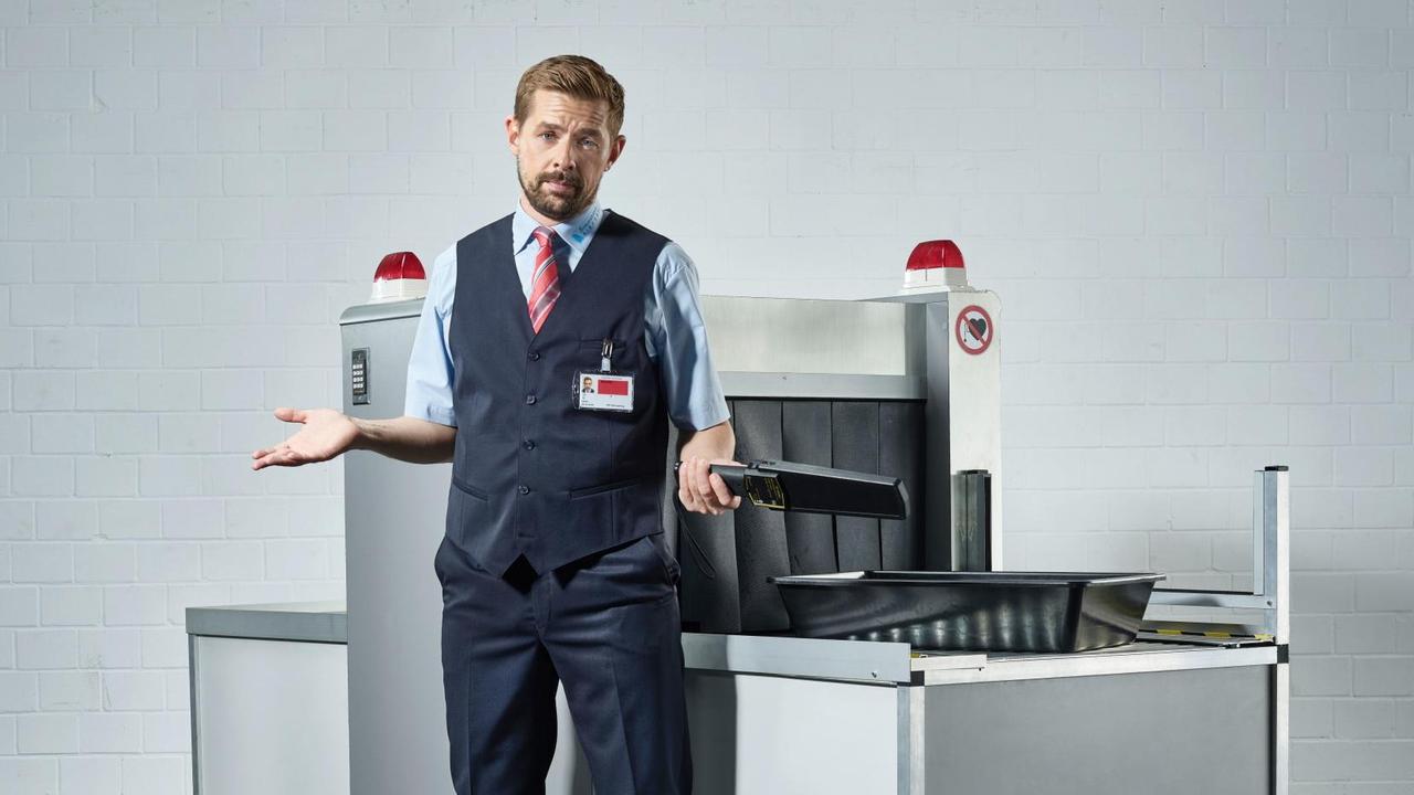 Klaas Heufer-Umlauf steht in Uniform und mit hilfloser Geste vor einem Gepäckscanner. Klaas Heufer-Umlauf steht in Uniform und mit hilfloser Geste vor einem Gepäckscanner.