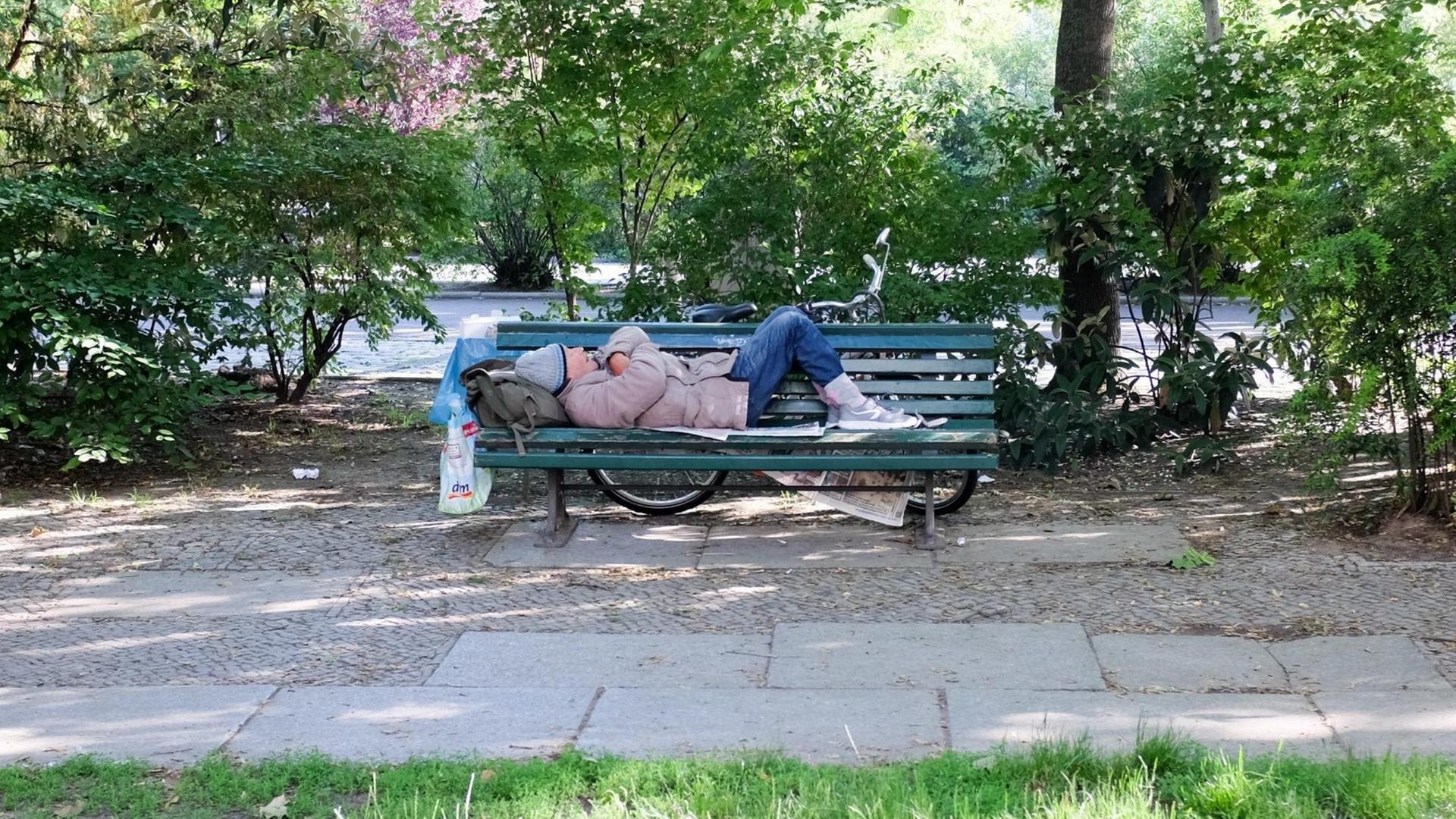 Auf einer Parkbank am Olivaer Platz schläft ein älterer Mann auf Zeitungen.