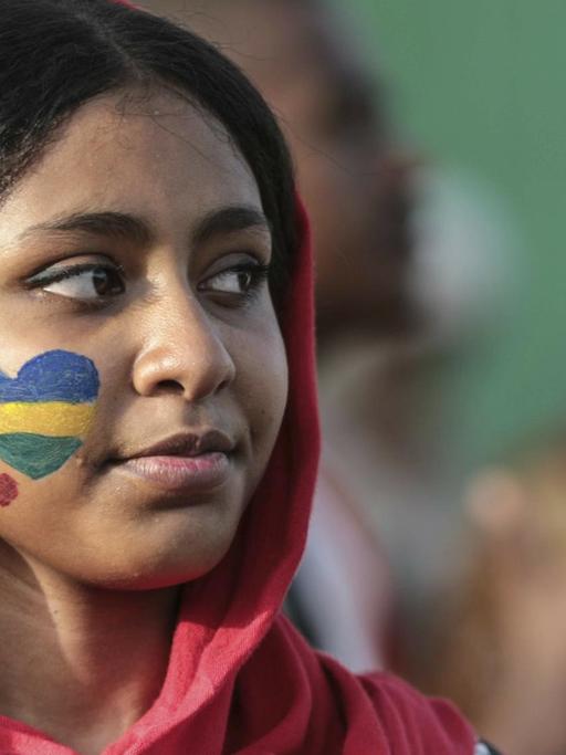 Aufnahme einer Frau mit einem geschminkten Herz auf der Wange in den Farben der alten sudanesischen Flagge.