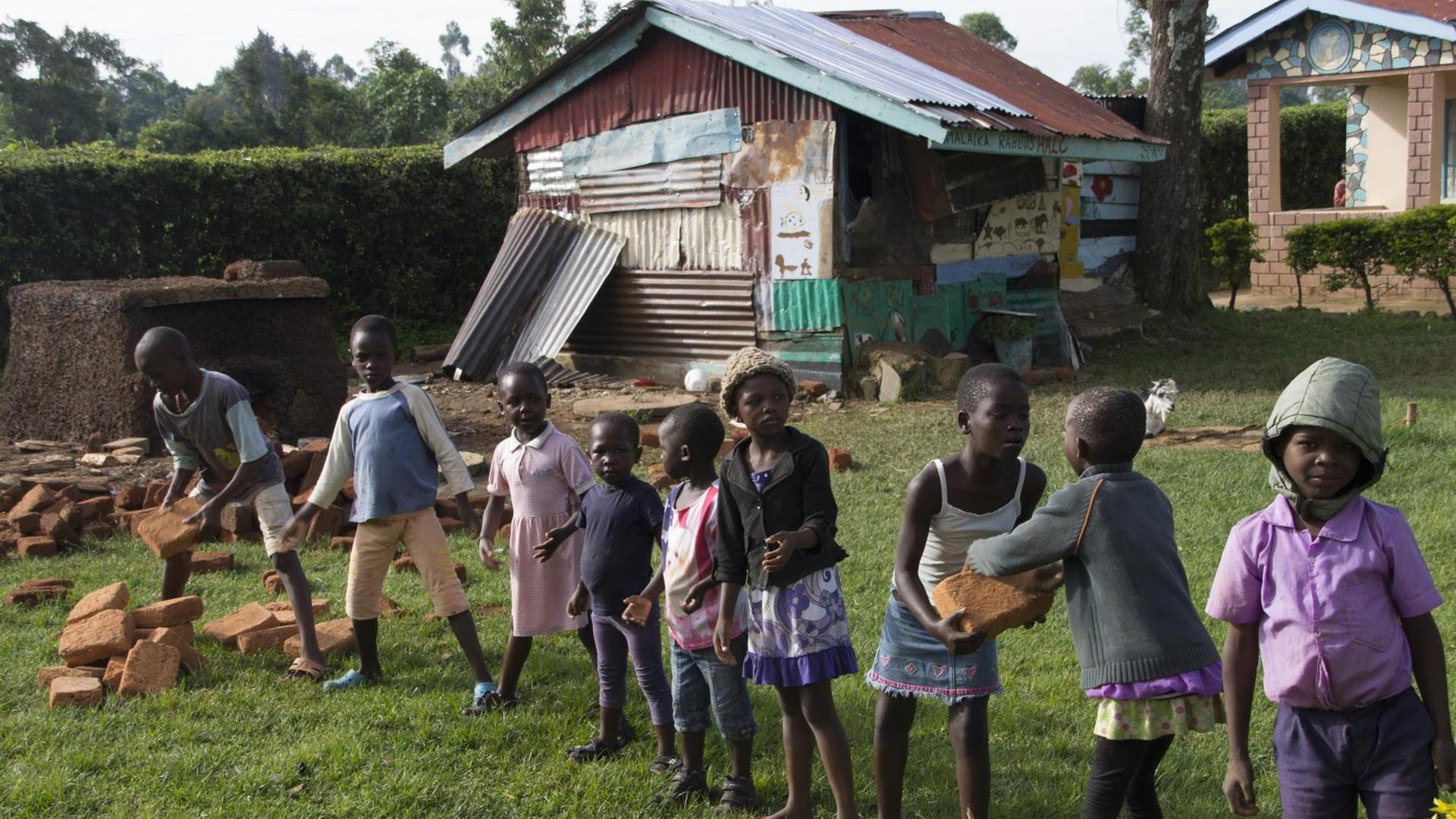 Kleine afrikanische Kinder haben sich in einer Reihe aufgestellt und bilden eine Kette, mittels derer Ziegelsteine für den Bau der Mädchentoiletten transportiert werden. Kleine afrikanische Kinder haben sich in einer Reihe aufgestellt und bilden eine Kette, mittels derer Ziegelsteine für den Bau der Mädchentoiletten transportiert werden.