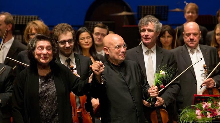 Die Pianistin und ein Dirigent erhalten vor dem Orchester stehend Beifall. Blumen liegen auf dem Flügel. Die Pianistin und ein Dirigent erhalten vor dem Orchester stehend Beifall. Blumen liegen auf dem Flügel.