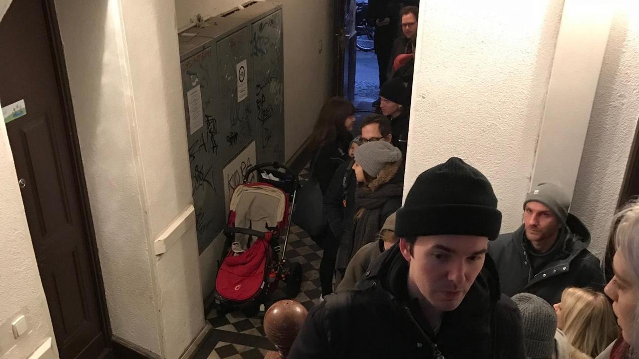 Eine lange Schlange von Wartenden im Treppenhaus einer Berliner Wohnung.