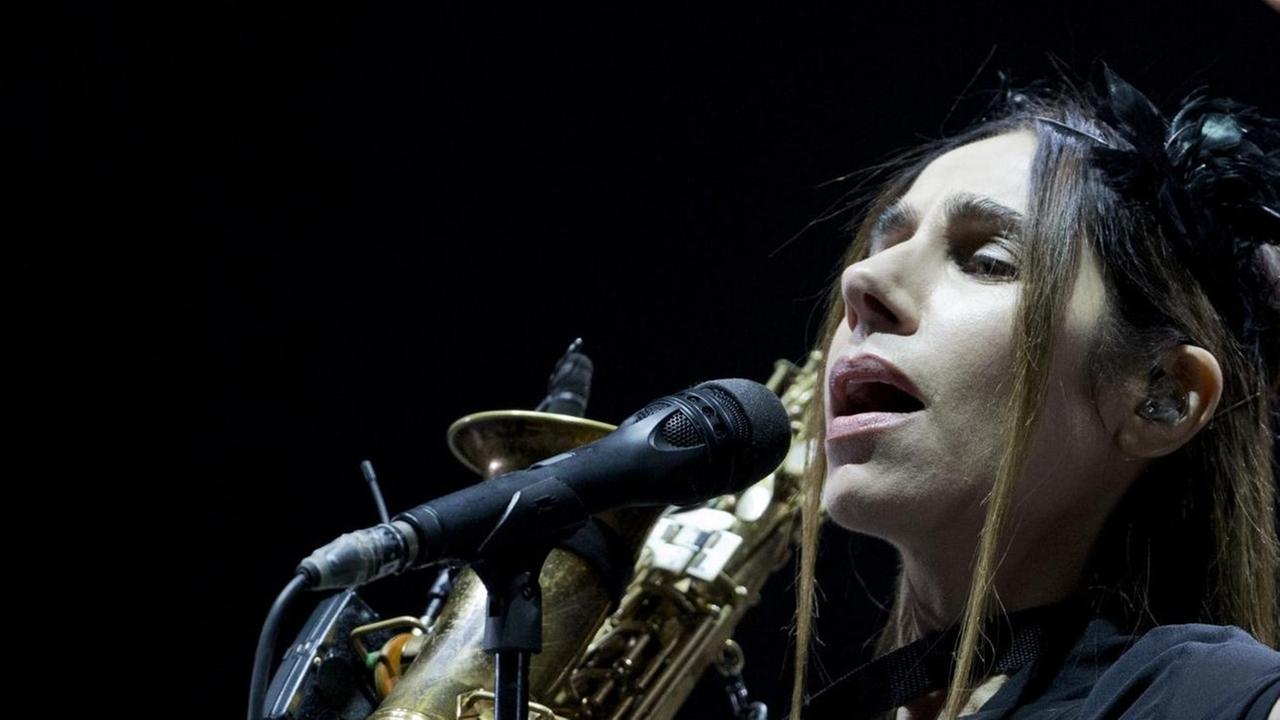 PJ Harvey steht vor einem Mikrophon mit einem Saxophon in der Hand. PJ Harvey steht vor einem Mikrophon mit einem Saxophon in der Hand.