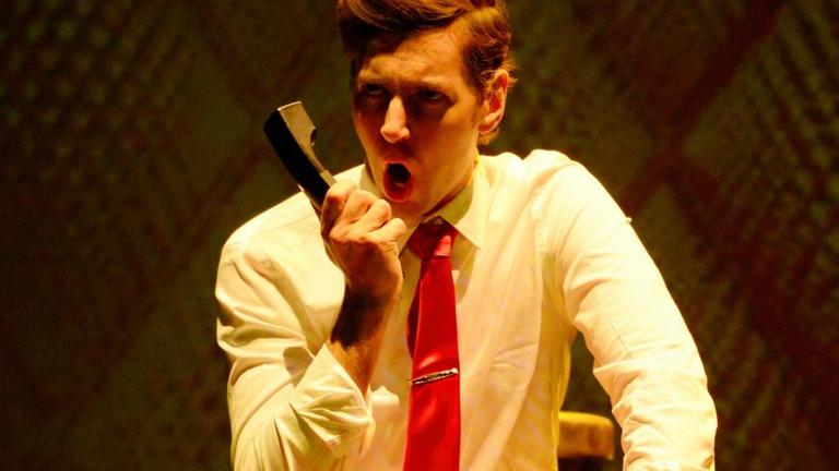 Ein Mann in weißem Hemd und roter Krawatte brüllt in einen Telefonhörer.