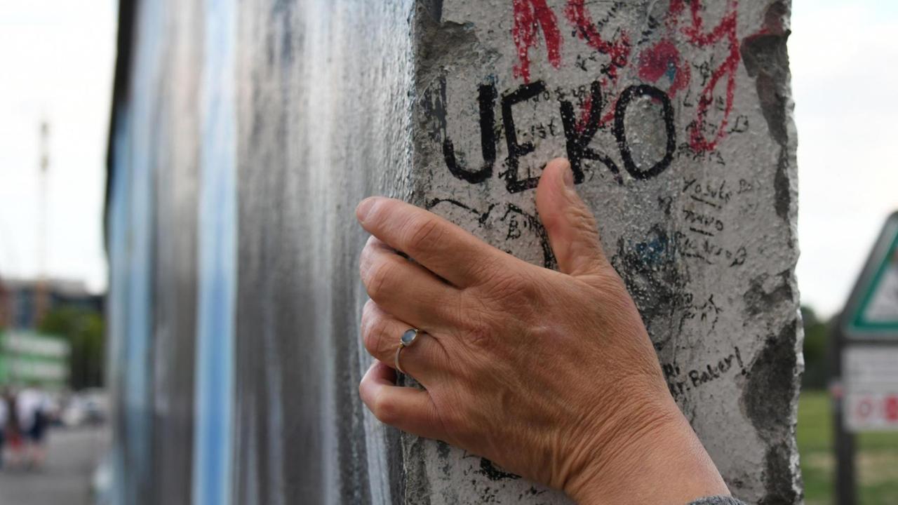 Eine Hand ruht auf einem Teil der Berliner Mauer.