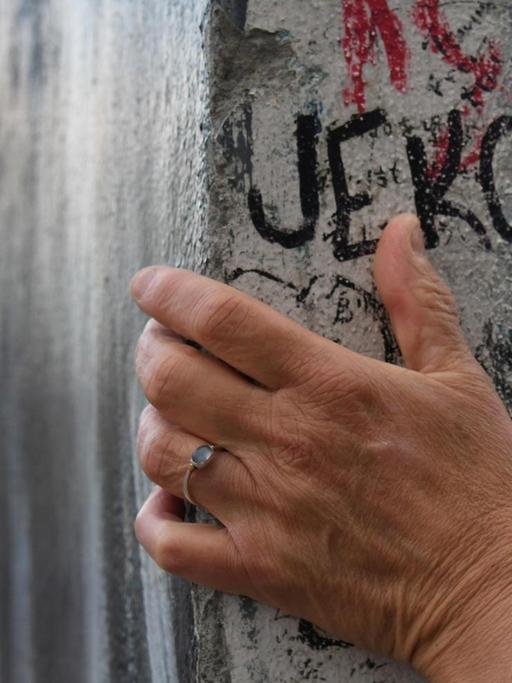 Eine Hand ruht auf einem Teil der Berliner Mauer.