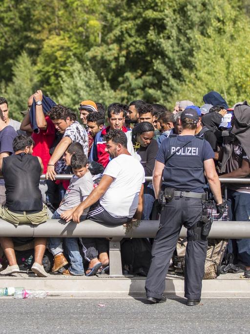 Zahlreiche Flüchtlinge warten am Grenzübergang zwischen Österreich und Deutschland in Freilassing (Bayern) darauf, nach Deutschland zu gelangen. Polizisten stehen vor und neben ihnen.