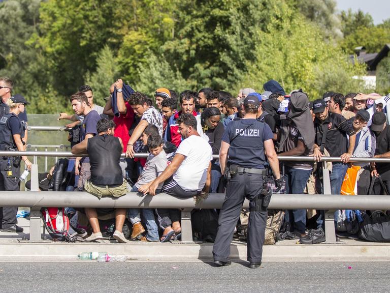 Zahlreiche Flüchtlinge warten am Grenzübergang zwischen Österreich und Deutschland in Freilassing (Bayern) darauf, nach Deutschland zu gelangen. Polizisten stehen vor und neben ihnen.