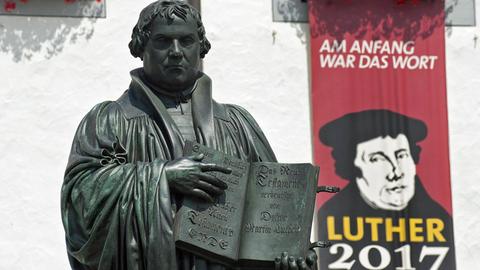 Denkmal des Reformators Martin Luther (1483 - 1546) mit der von ihm ins Deutsche übersetzten Bibel in der Hand auf dem Marktplatz der Lutherstadt Wittenberg. Im Hintergrund hängt am Rathaus ein Transparent zum Reformationsjubiläum Luther 2017.
