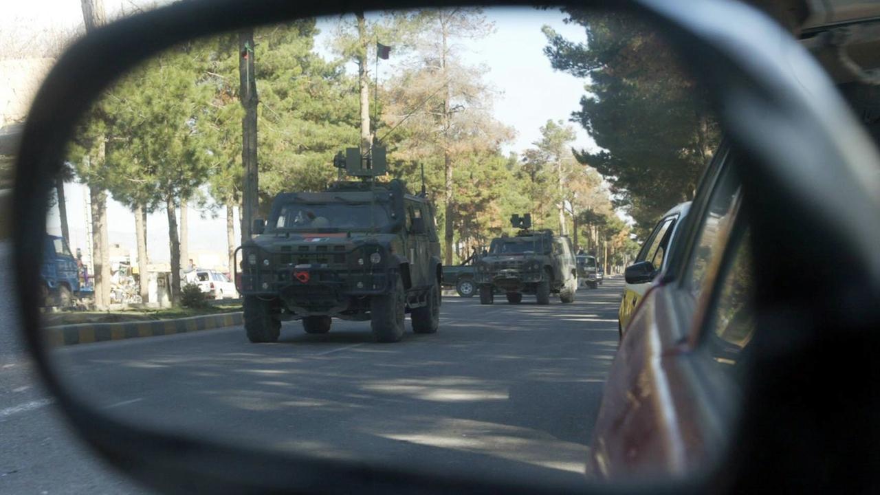 Im Rückspiegel eines Autos sind Militärfahrzeuge zu sehen.