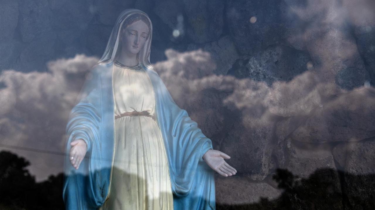 Eine Jungfrau Maria Statue hinter Glas, in dem sich der Himmel spiegelt. Eine Jungfrau Maria Statue hinter Glas, in dem sich der Himmel spiegelt.