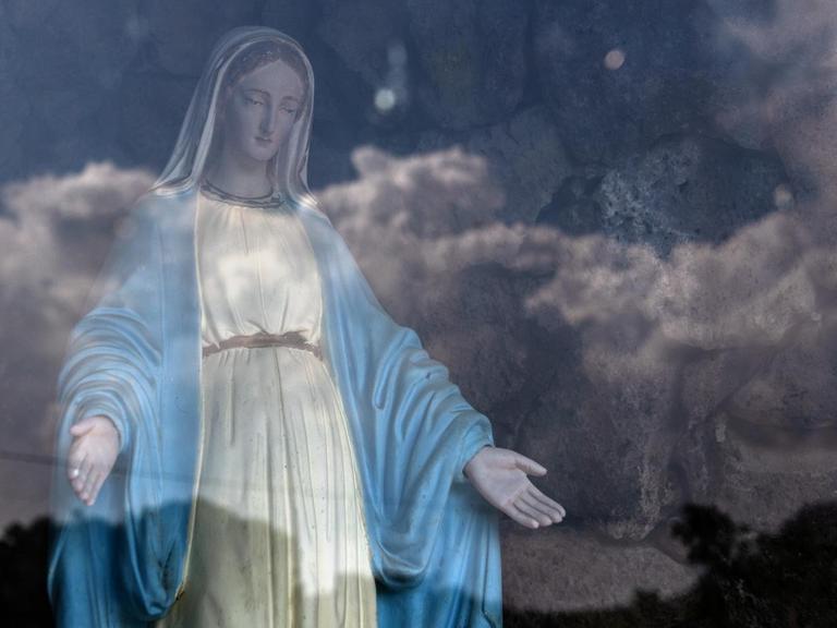 Eine Jungfrau Maria Statue hinter Glas, in dem sich der Himmel spiegelt.