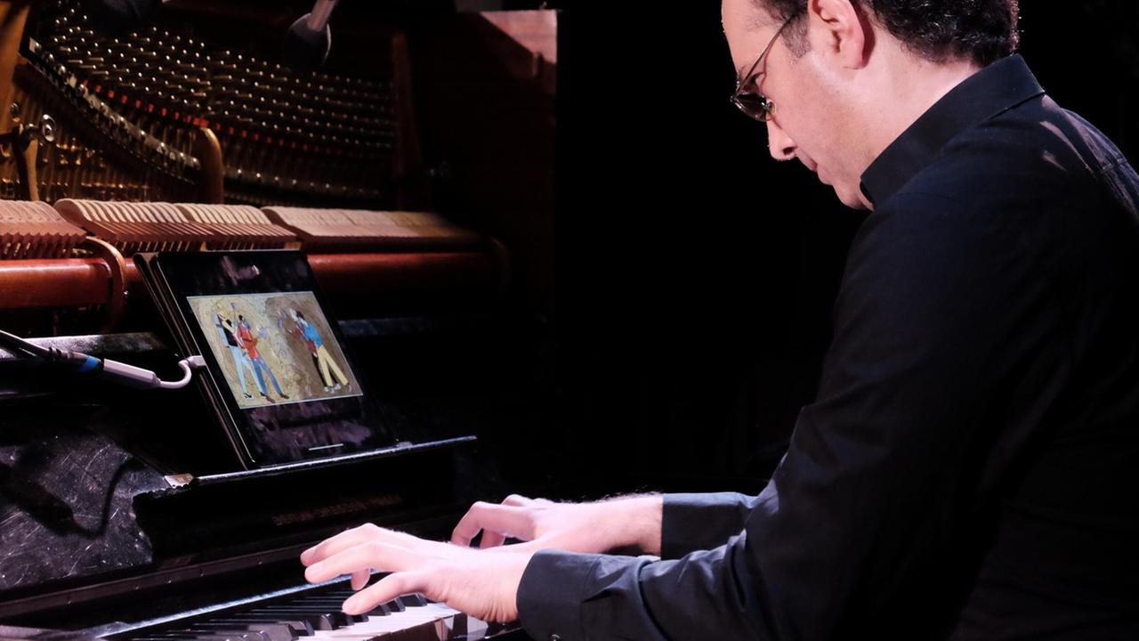 Ein Klavierspieler sitz an seinem Instrument, im Notenständer befindet sich ein Tablet, auf dessen Bildschirm ist ein Comic zu sehen.