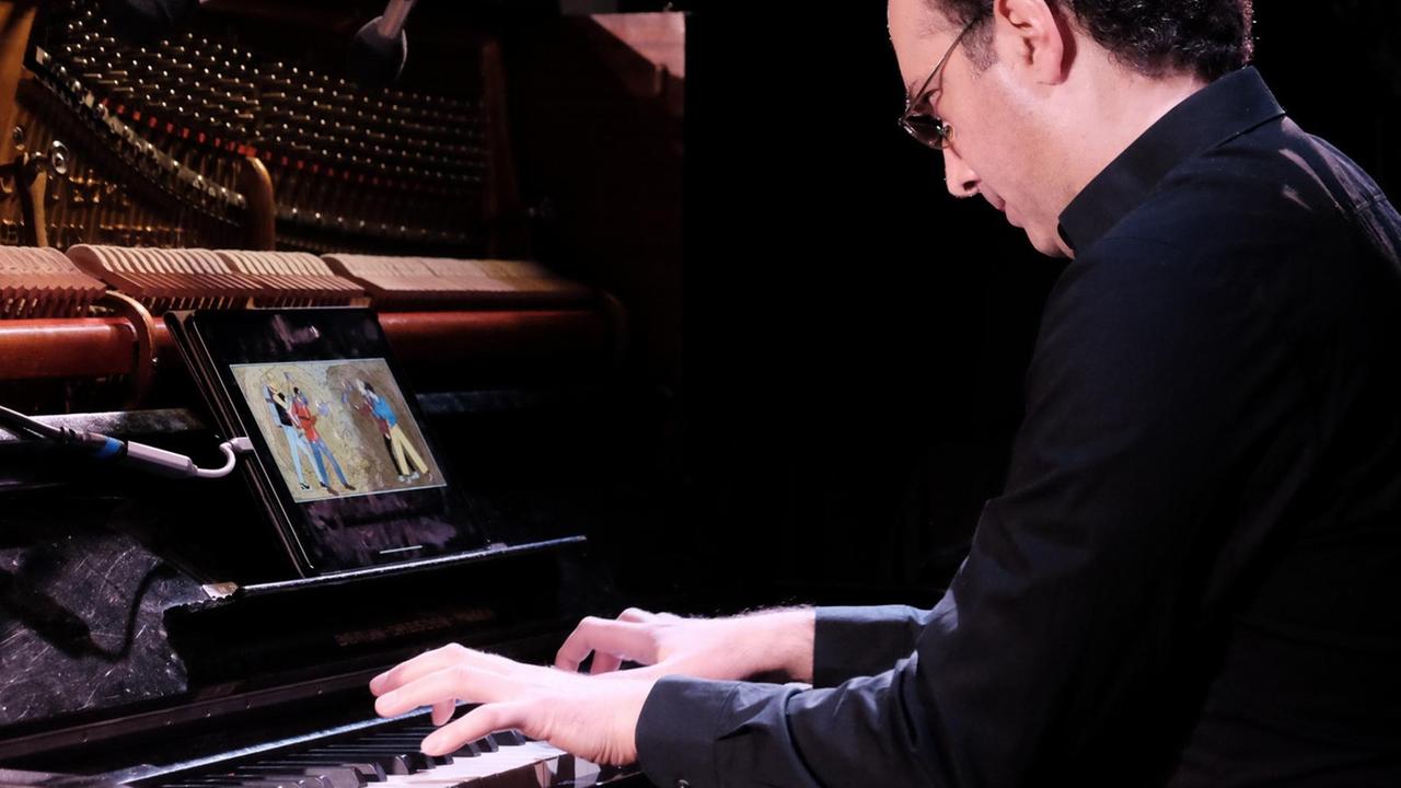 Ein Klavierspieler sitz an seinem Instrument, im Notenständer befindet sich ein Tablet, auf dessen Bildschirm ist ein Comic zu sehen. Ein Klavierspieler sitz an seinem Instrument, im Notenständer befindet sich ein Tablet, auf dessen Bildschirm ist ein Comic zu sehen.