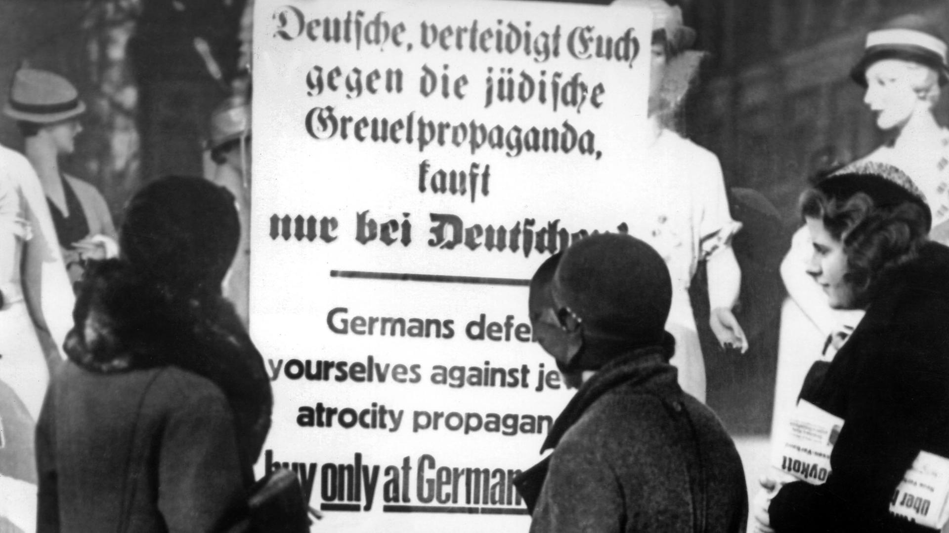Drei deutsche Frauen lesen im April 1933 ein Plakat am Schaufenster eines Geschäfts, das zum Boykott von jüdischen Geschäften aufruft: "Deutsche, verteidigt Euch gegen die jüdische Greuelpropaganda, kauft nur bei Deutschen!"