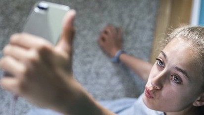 Ein blondes attraktives Mädchen sitzt in ihrem Zimmer auf dem Boden und macht Selfies Ein blondes attraktives Mädchen sitzt in ihrem Zimmer auf dem Boden und macht Selfies
