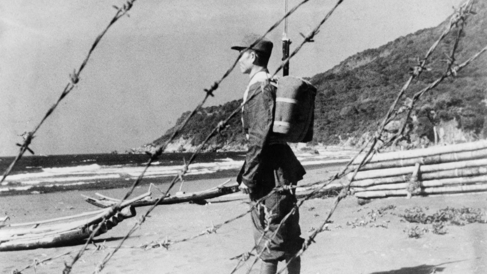Ein bewaffneter Soldat steh an einem Strand. Um ihn herum Stacheldraht. Ein bewaffneter Soldat steh an einem Strand. Um ihn herum Stacheldraht.