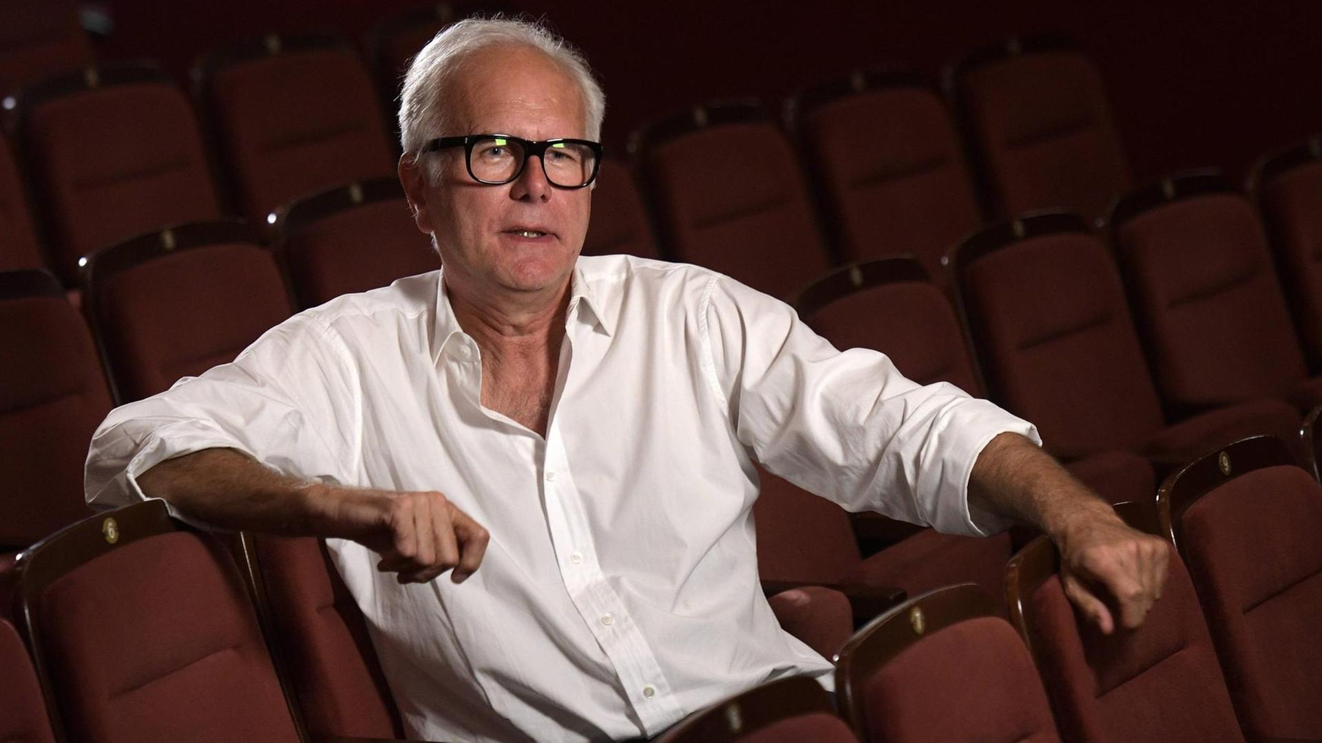 Harald Schmidt trägt ein weißes Hemd und sitzt auf die Bühne blickend alleine im Parkett eines Theaters. Harald Schmidt trägt ein weißes Hemd und sitzt auf die Bühne blickend alleine im Parkett eines Theaters.
