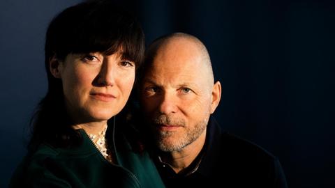 Porträt von Charlotte Roche und Martin Keß-Roche vor dunklem Hintergrund.